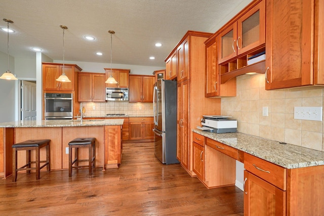 kitchen featuring a kitchen bar, appliances with stainless steel finishes, tasteful backsplash, brown cabinets, and dark wood-style floors