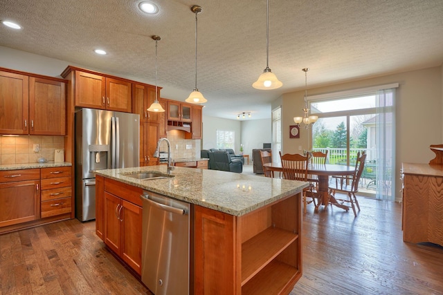kitchen with brown cabinets, a sink, a textured ceiling, stainless steel appliances, and tasteful backsplash