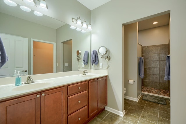 bathroom with double vanity, tiled shower, a sink, and tile patterned flooring
