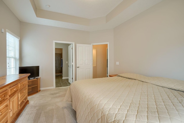 bedroom featuring baseboards, light colored carpet, a tray ceiling, and ensuite bath