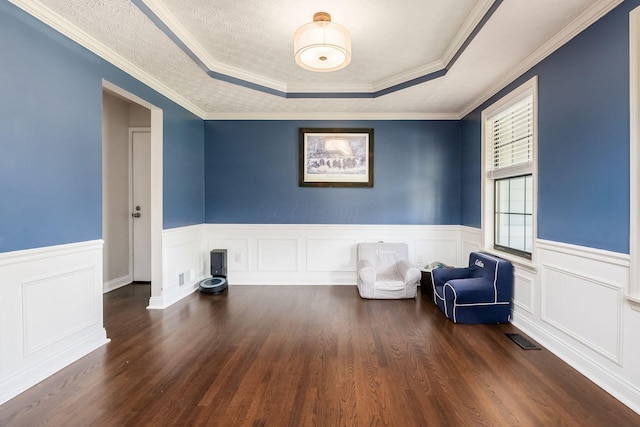unfurnished room featuring dark wood-style flooring, wainscoting, visible vents, crown molding, and a raised ceiling