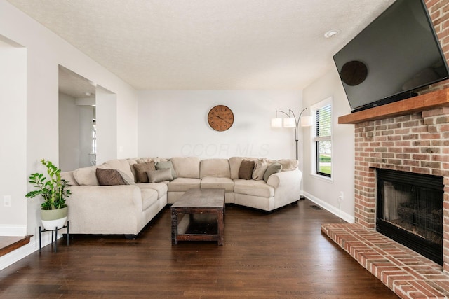 living room featuring dark wood finished floors, a brick fireplace, baseboards, and visible vents