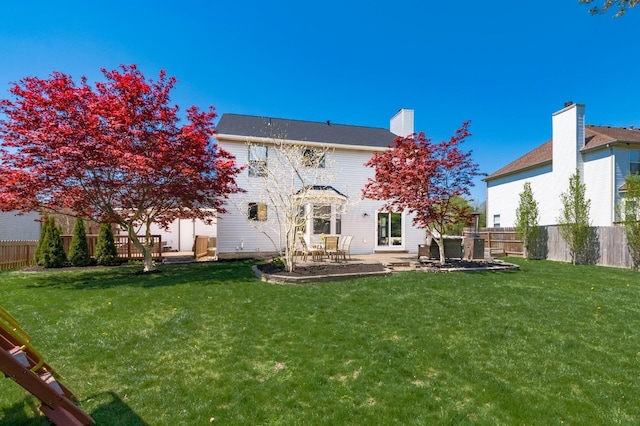 back of property with a fenced backyard, a chimney, a patio, and a lawn