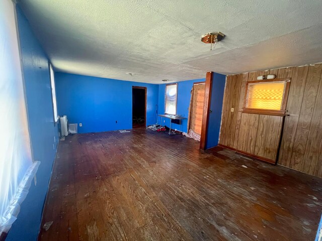 unfurnished living room featuring hardwood / wood-style flooring, radiator, a textured ceiling, and wooden walls
