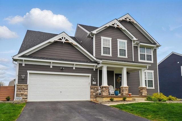 craftsman-style house featuring a porch, fence, a garage, driveway, and stone siding