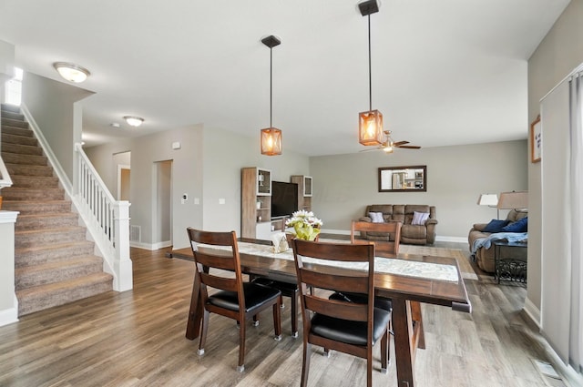 dining room featuring ceiling fan, baseboards, light wood-style flooring, and stairs