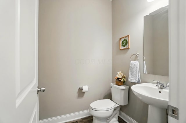 bathroom with baseboards, wood finished floors, toilet, and a sink