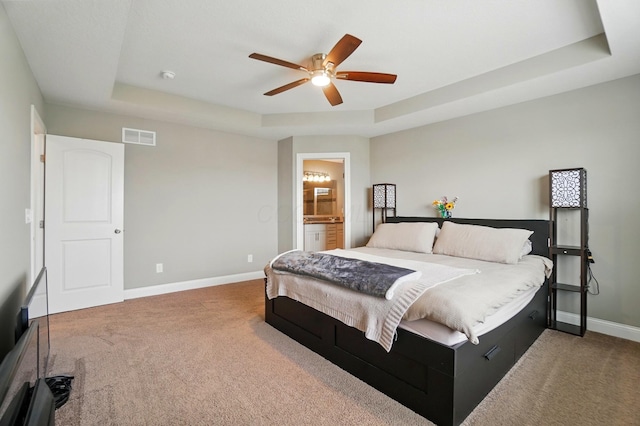 carpeted bedroom featuring visible vents, a tray ceiling, baseboards, a ceiling fan, and ensuite bath