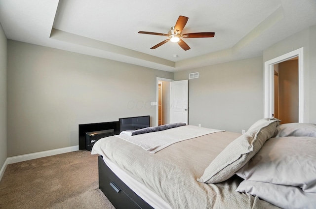 carpeted bedroom with a raised ceiling, visible vents, a ceiling fan, and baseboards