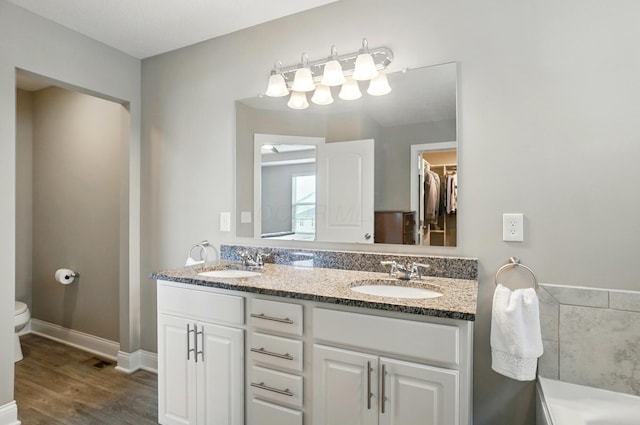 full bathroom with wood finished floors, toilet, a walk in closet, and a sink