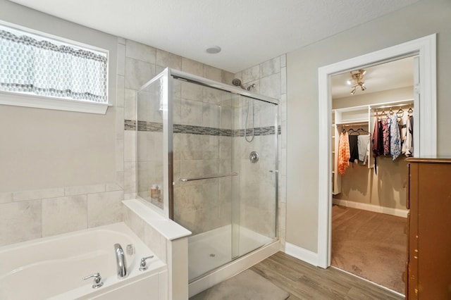 full bathroom with a spacious closet, wood finished floors, a shower stall, and a bath