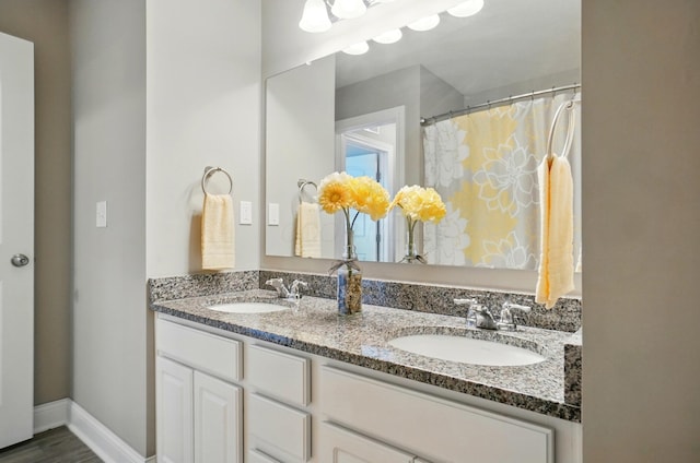 bathroom featuring double vanity, a sink, wood finished floors, and baseboards