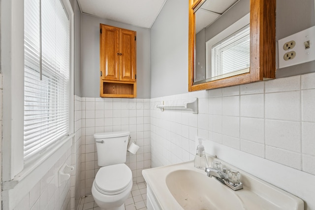 half bathroom featuring a sink, wainscoting, toilet, and tile walls