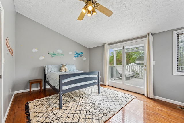 bedroom featuring access to outside, a textured ceiling, multiple windows, and hardwood / wood-style flooring