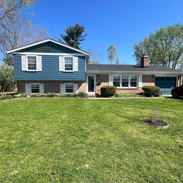 split level home with a chimney, an attached garage, brick siding, and a front lawn