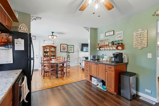 kitchen with a ceiling fan, freestanding refrigerator, brown cabinetry, and dark wood finished floors