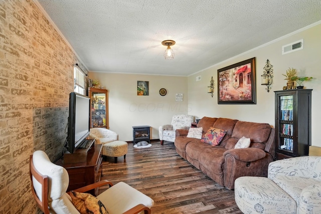 living room with crown molding, a wood stove, visible vents, dark wood-style flooring, and brick wall
