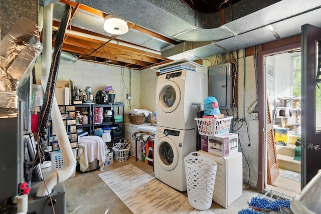laundry room with concrete block wall, electric panel, and stacked washing maching and dryer