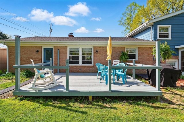 rear view of house with a deck, a chimney, outdoor dining area, a lawn, and brick siding