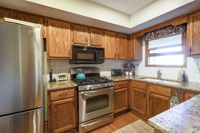 kitchen with backsplash, light wood finished floors, stainless steel appliances, and a sink