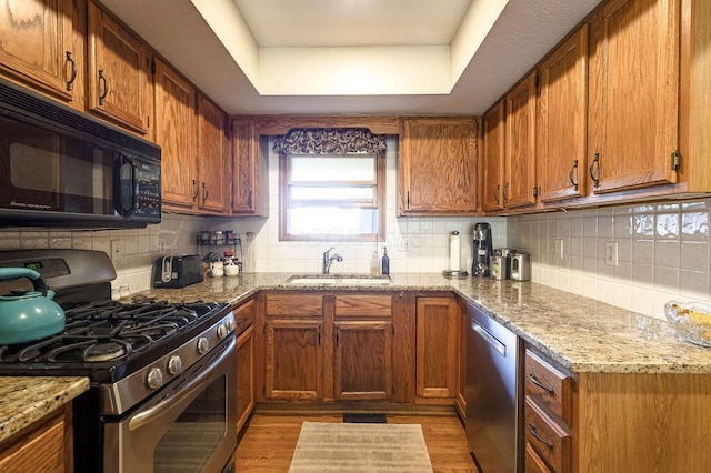 kitchen featuring stainless steel appliances, backsplash, a raised ceiling, a sink, and light wood-style floors