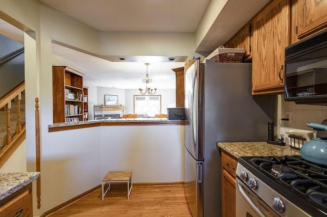 kitchen with stainless steel range with gas cooktop, hanging light fixtures, brown cabinets, black microwave, and light wood finished floors