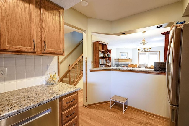kitchen featuring light wood-style flooring, freestanding refrigerator, an inviting chandelier, decorative backsplash, and brown cabinets