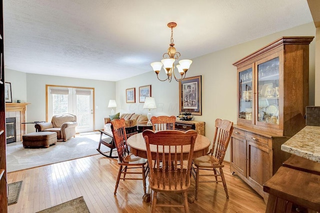 dining area featuring light wood finished floors, a tile fireplace, and a notable chandelier