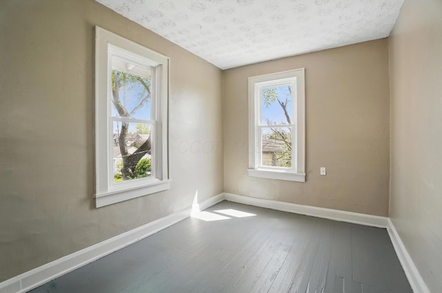 spare room with baseboards, a textured ceiling, a wealth of natural light, and hardwood / wood-style floors