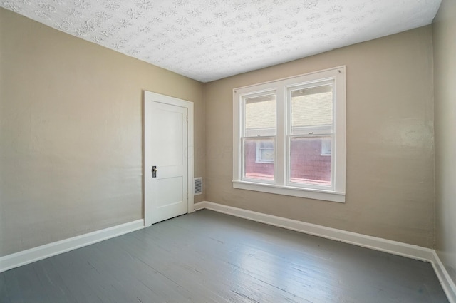 unfurnished room with a textured ceiling, baseboards, visible vents, and wood finished floors