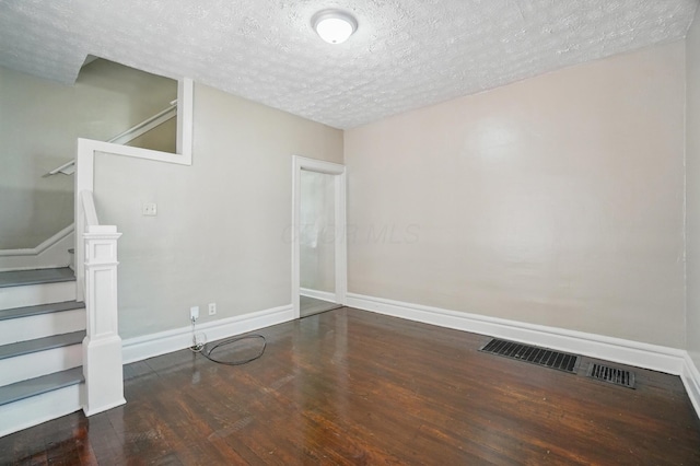 interior space with a textured ceiling, stairs, baseboards, wood finished floors, and visible vents