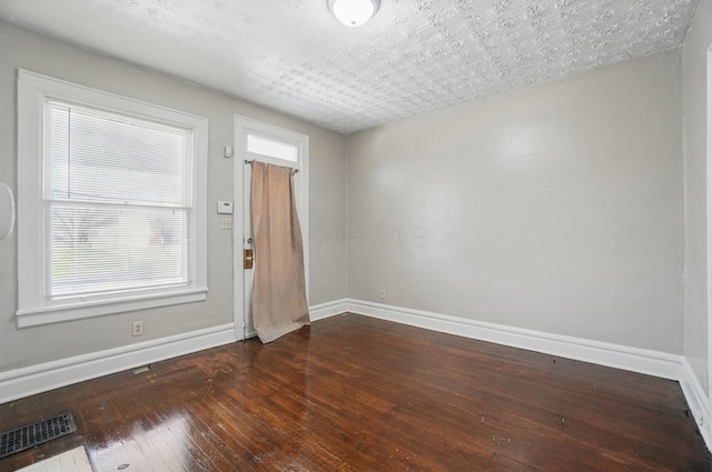 spare room featuring baseboards, dark wood finished floors, and visible vents