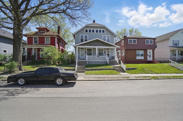 american foursquare style home featuring a porch, a chimney, and a front yard
