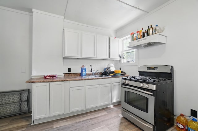 kitchen featuring stainless steel gas stove, white cabinetry, a sink, under cabinet range hood, and light wood-style flooring