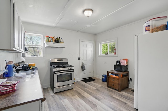 kitchen featuring freestanding refrigerator, black microwave, light wood-style floors, stainless steel gas range oven, and under cabinet range hood
