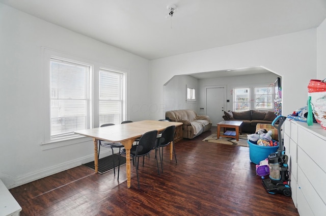 dining space featuring arched walkways, baseboards, and wood finished floors