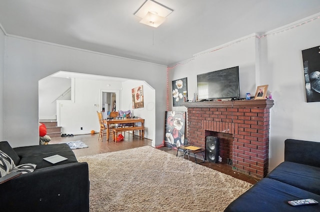 living area with crown molding, a brick fireplace, wood finished floors, and stairway