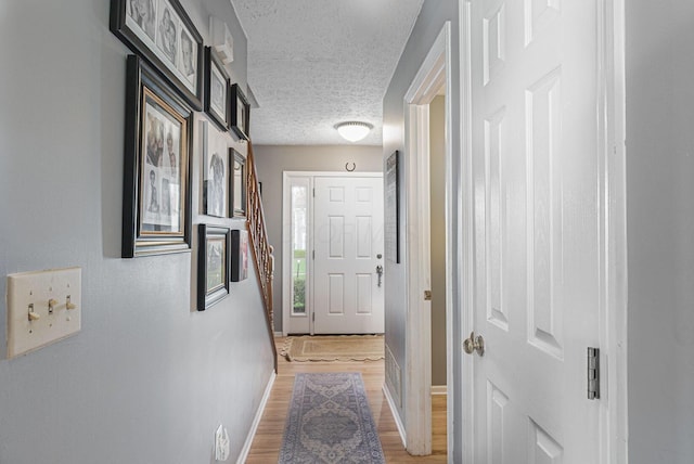 corridor featuring baseboards, a textured ceiling, and light wood-style flooring
