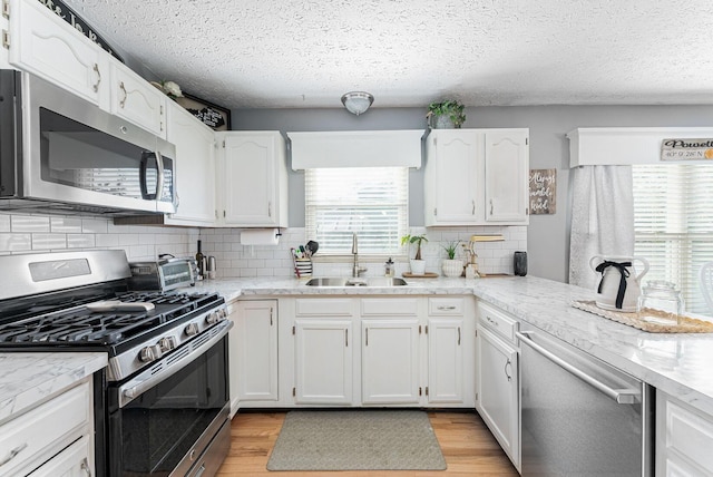 kitchen with light wood-style flooring, white cabinetry, stainless steel appliances, and a sink