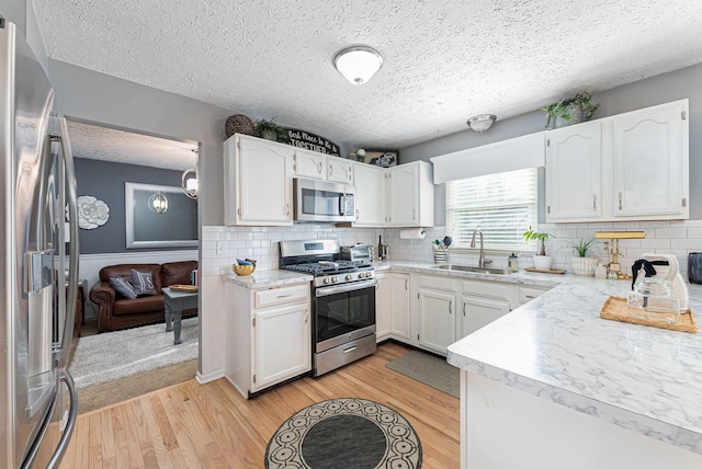 kitchen with white cabinets, light wood finished floors, a sink, a textured ceiling, and appliances with stainless steel finishes