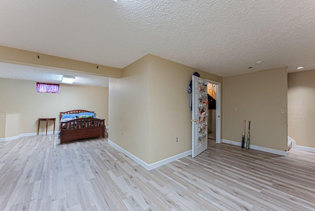 bedroom with baseboards, a textured ceiling, and light wood-style flooring