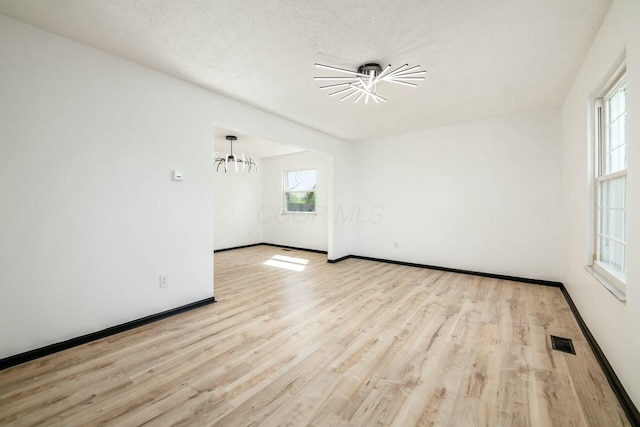 spare room featuring a notable chandelier, visible vents, wood finished floors, and baseboards