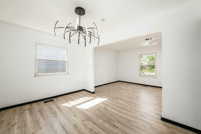 empty room with wood finished floors, a chandelier, visible vents, and baseboards