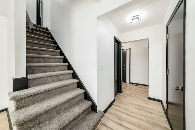 staircase featuring a textured ceiling, wood finished floors, and baseboards