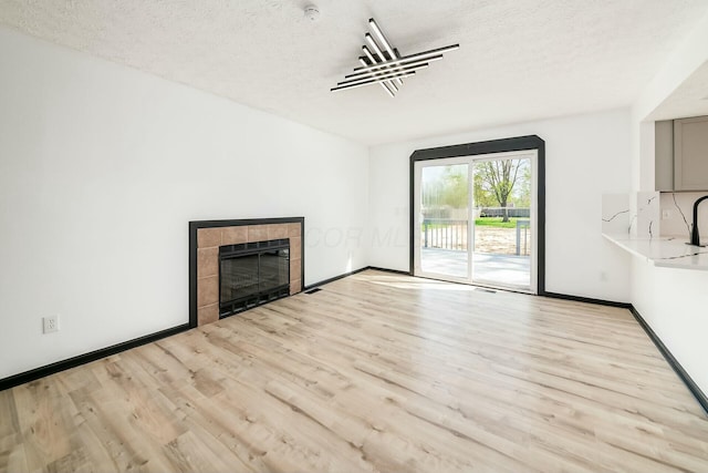 unfurnished living room featuring a fireplace, a textured ceiling, light wood-type flooring, and baseboards