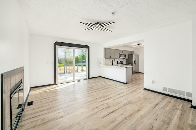 unfurnished living room with a chandelier, visible vents, light wood-type flooring, and a textured ceiling
