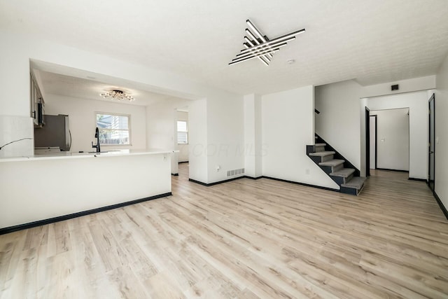 unfurnished living room with stairs, light wood-style flooring, a sink, baseboards, and visible vents