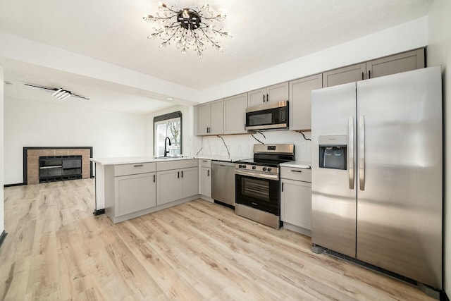 kitchen with a sink, stainless steel appliances, gray cabinets, light wood-type flooring, and a peninsula