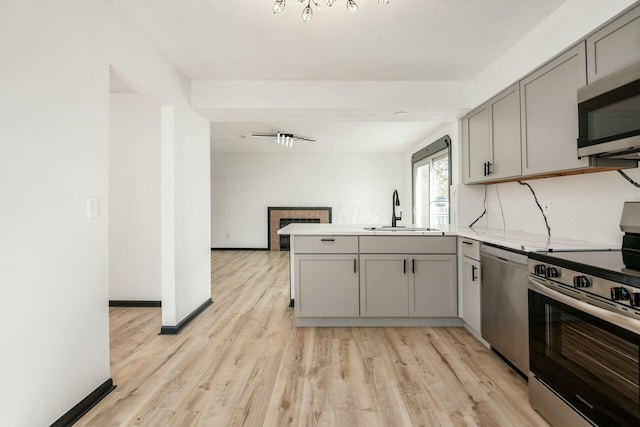 kitchen with a tile fireplace, a sink, stainless steel appliances, gray cabinets, and a peninsula