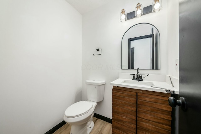 half bathroom featuring baseboards, wood finished floors, toilet, and vanity